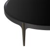 A sophisticated coffee table by Eichholtz with a round black bevelled glass top, bronze frame and brass accents on it's tapered feet