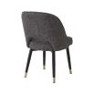 A trendy and chic pair of upholstered dining chairs with a curved back, black legs and brass feet