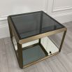 A contemporary side table by Eichholtz with a brushed brass frame, smoked glass top and mirrored glass bottom shelf