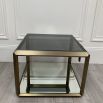 A contemporary side table by Eichholtz with a brushed brass frame, smoked glass top and mirrored glass bottom shelf