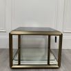 A contemporary side table by Eichholtz with a brushed brass frame, smoked glass top and mirrored glass bottom shelf