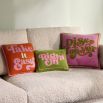 A hand-embroidered cushion with playful, retro-inspired bumper sticker sentiments, crafted with couture materials and velvet backing.