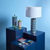 A maximalist inspired table lamp with blue archways   decorating the base, gold accents and a white paper shade