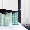 An art deco patterned cushion with blue, green and white designs and white piping