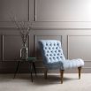 A luxury occasional chair with a blue, silky upholstery and buttoned back