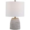 This table lamp has a concrete base with white etching, brushed nickel accents, and a light beige linen shade, offering modern sophistication and understated elegance.