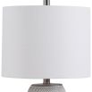 This table lamp has a concrete base with white etching, brushed nickel accents, and a light beige linen shade, offering modern sophistication and understated elegance.
