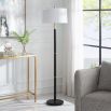 The Troy Floor Lamp, featuring a minimalist design with gold rings along its slender body, is finished with a subtly tapered hardback shade in soft white linen with delicate slubbing, exuding refined elegance.