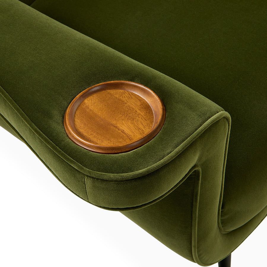 The Pierre Lounge Chair features a swooping silhouette, emerald velvet upholstery, and a built-in wood coaster, making it a glamorous addition to any space.