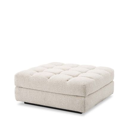 An ottoman upholstered in a boucle cream fabric mounted on a black base.