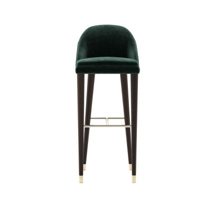 A luxurious bar stool with velvet upholstery and wooden legs with metallic details. Pictured in Vienna Green.