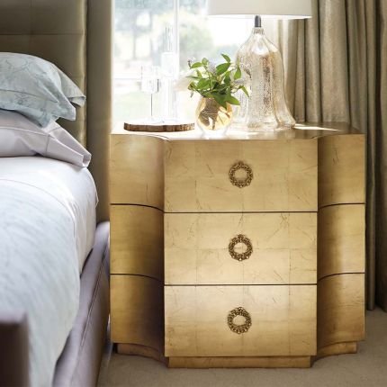 A golden bedside table with three drawers.