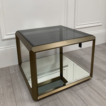 A contemporary side table by Eichholtz with a brushed brass frame, smoked glass top and mirrored glass bottom shelf