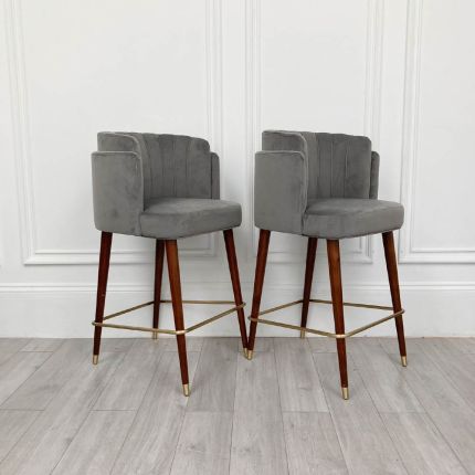 An elegantly glamorous bar chair with grey velvet upholstery and long lacquered legs with polished brass details 