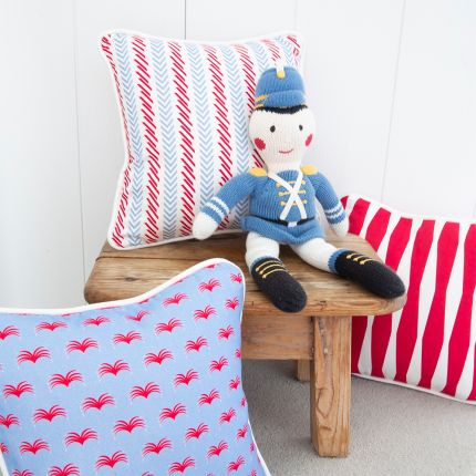A bright blue and red children's cushion with a lovely pattern and white piping  