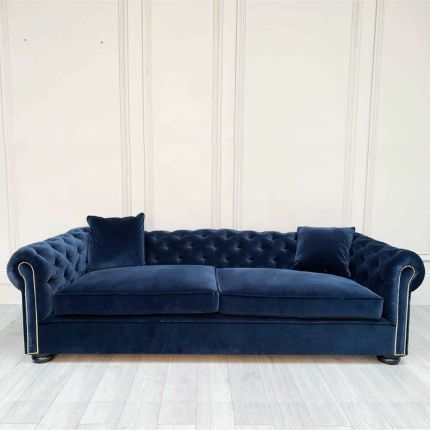 A luxurious sofa with a denim coloured velvet upholstery, deep buttoning and studding 