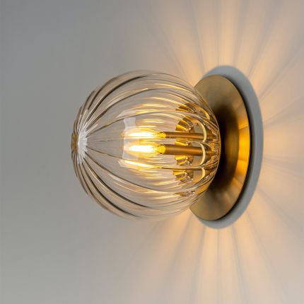 A luxury wall sconce by Schwung with a glamorous brass finish and elegant detailed clear glass bulb