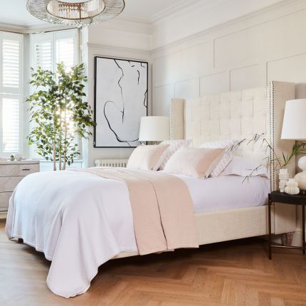 An elegant pale taupe linen kingsize bed with a tufted headboard and bronze-coloured studding